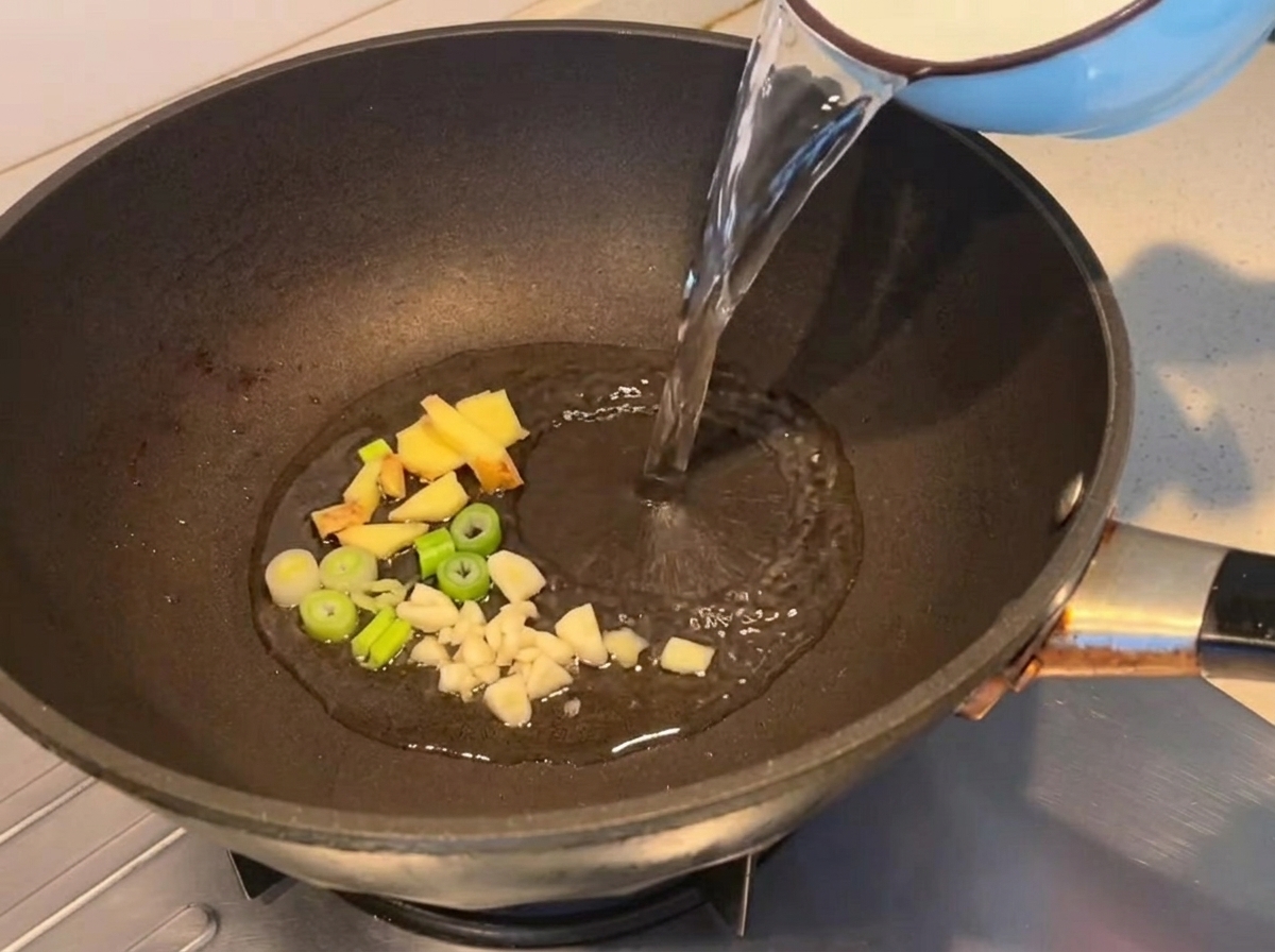 Water being poured into a pan with sautéed aromatics.