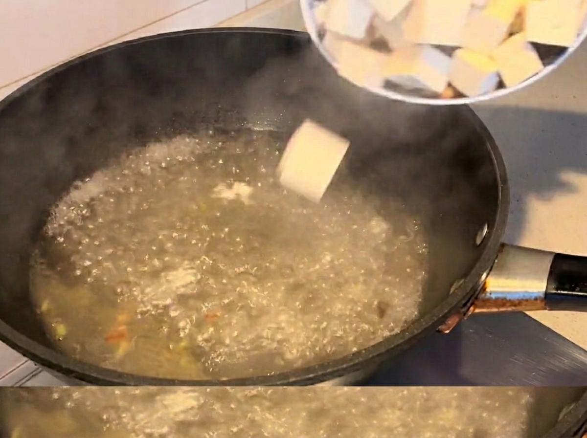 Tofu cubes and clams cooking in a boiling soup.