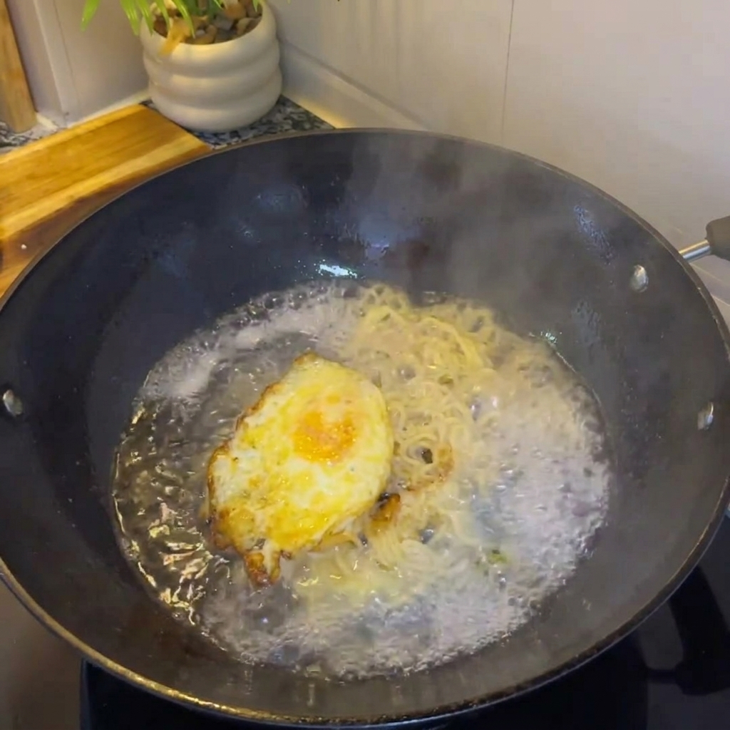 Hot water being poured into the wok with the egg and onions, creating a broth.