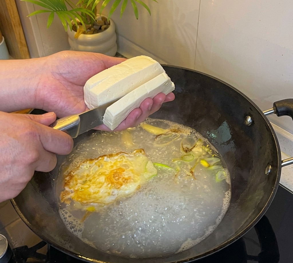 Tofu being sliced into cubes into the boiling soup base.