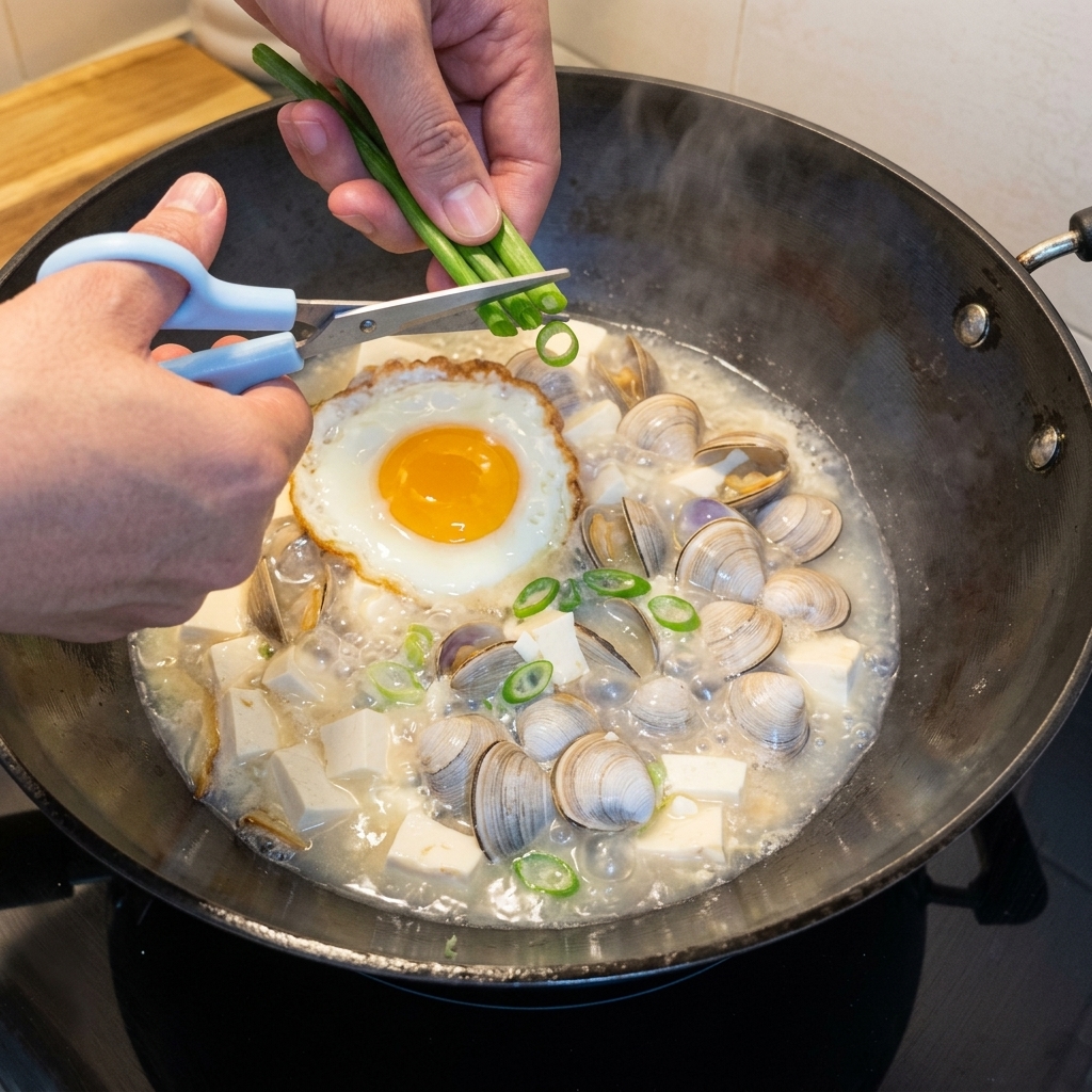 Freshly chopped green onions being sprinkled into a bubbling pot of tofu and clam soup.