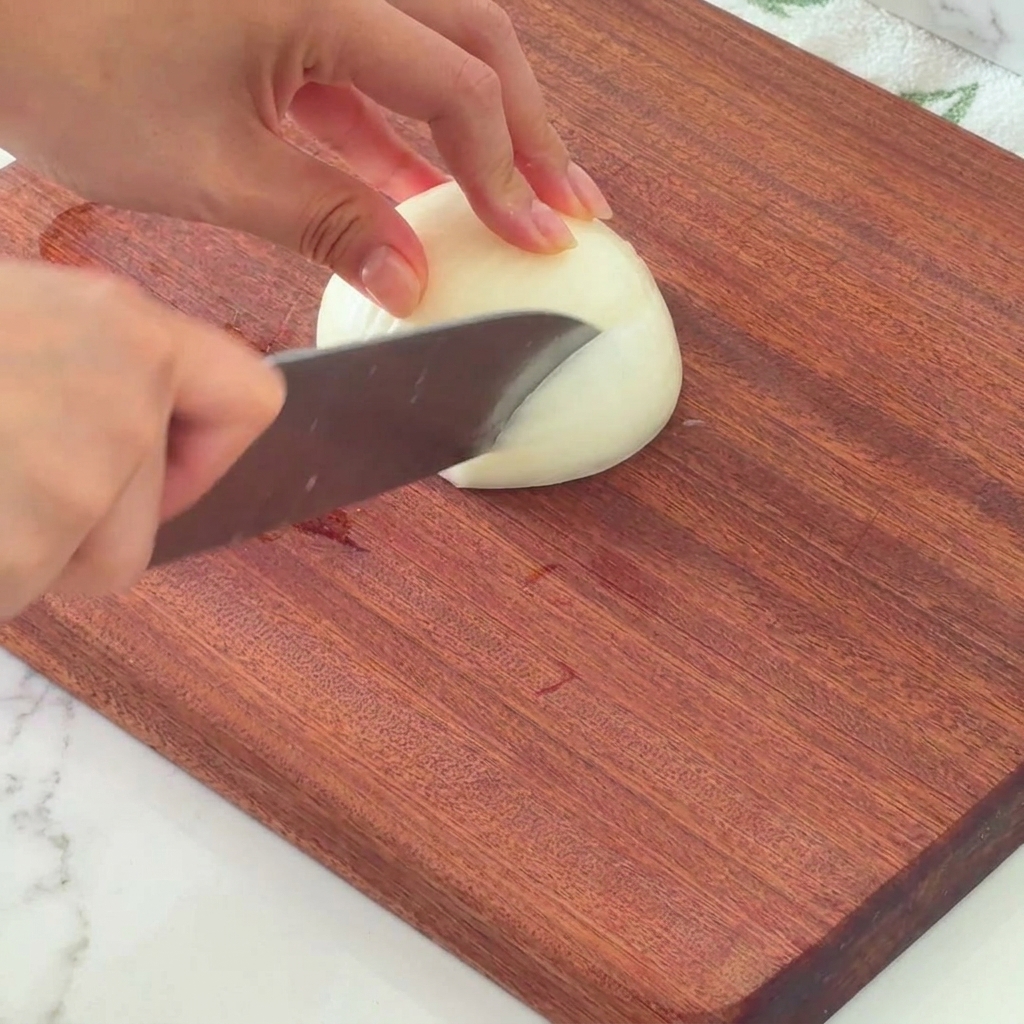 Half of a white onion being carefully diced on a wooden board.