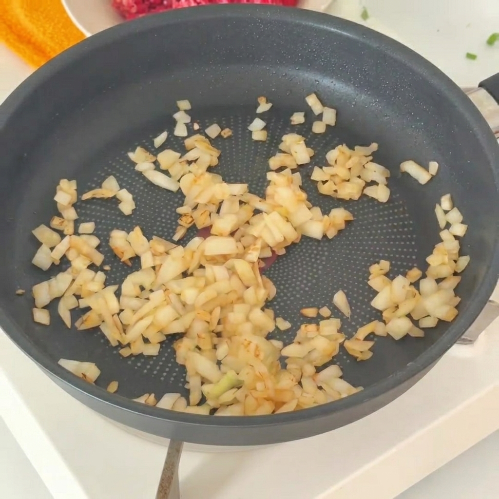 The sautéed onions being transferred into a bowl with fresh minced beef.
