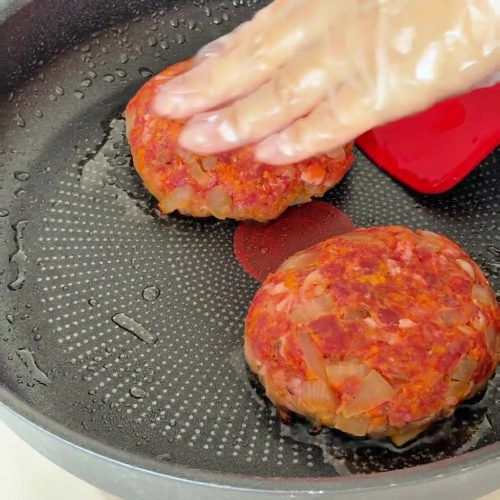 Hamburger patties in a pan being covered with a lid after flipping.