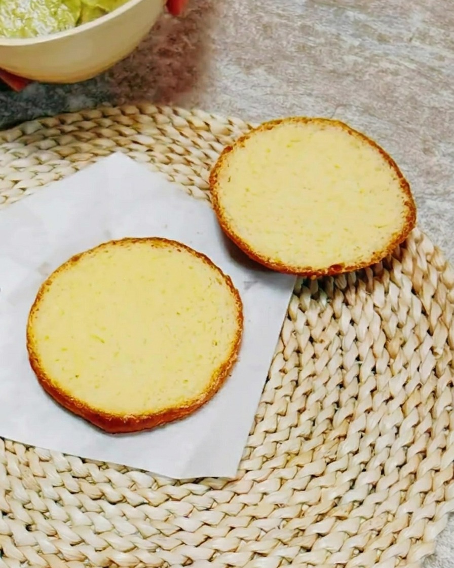The cut sides of a burger bun spread with a creamy, green herb-based sauce.