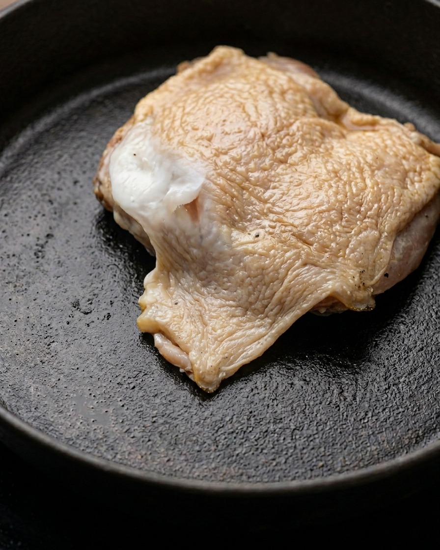 A piece of marinated chicken leg meat browning in a pan with melted butter.