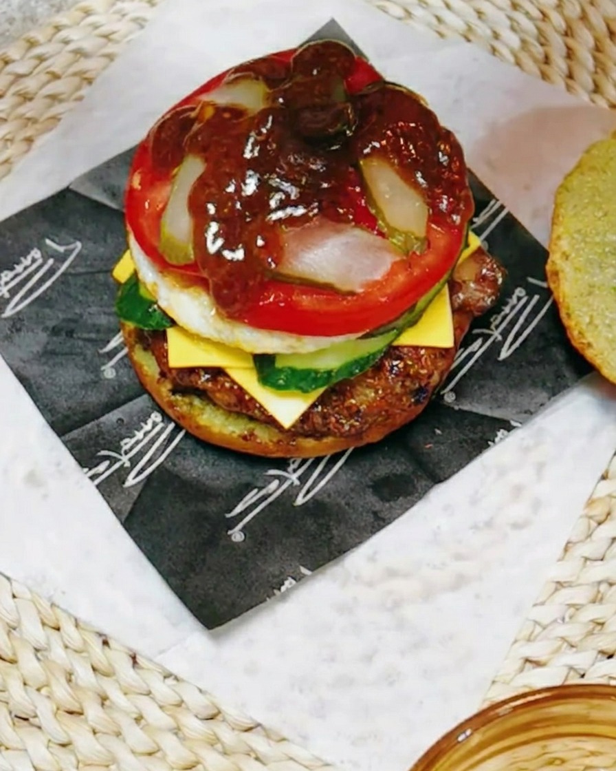 A close-up shot of the burger stack being drizzled with a dark, savory teriyaki-based sauce mixed with lemon juice.