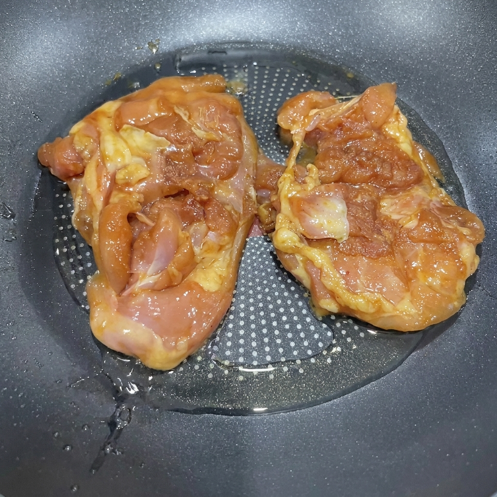Marinated chicken thighs sizzling in a pan with hot oil.