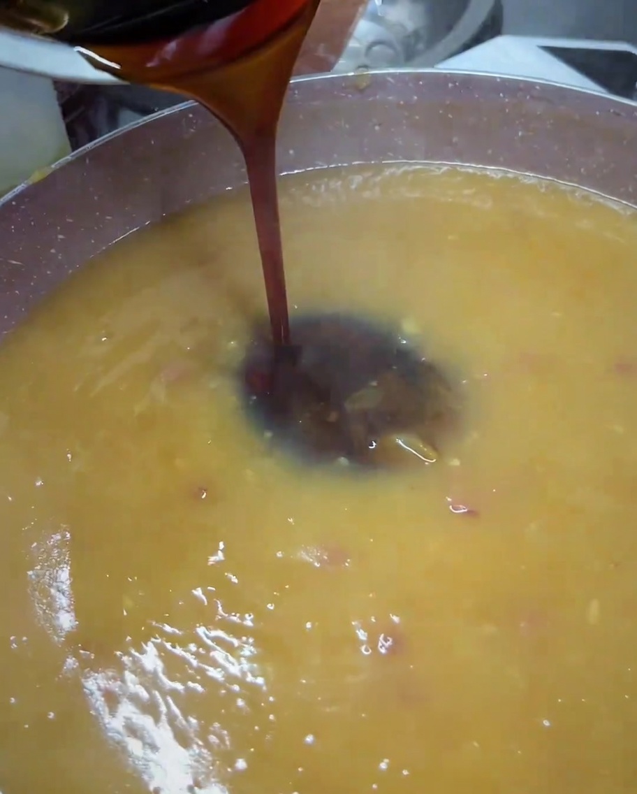 Dark teriyaki sauce being poured from a small bowl into a pan of blended golden-brown sauce.