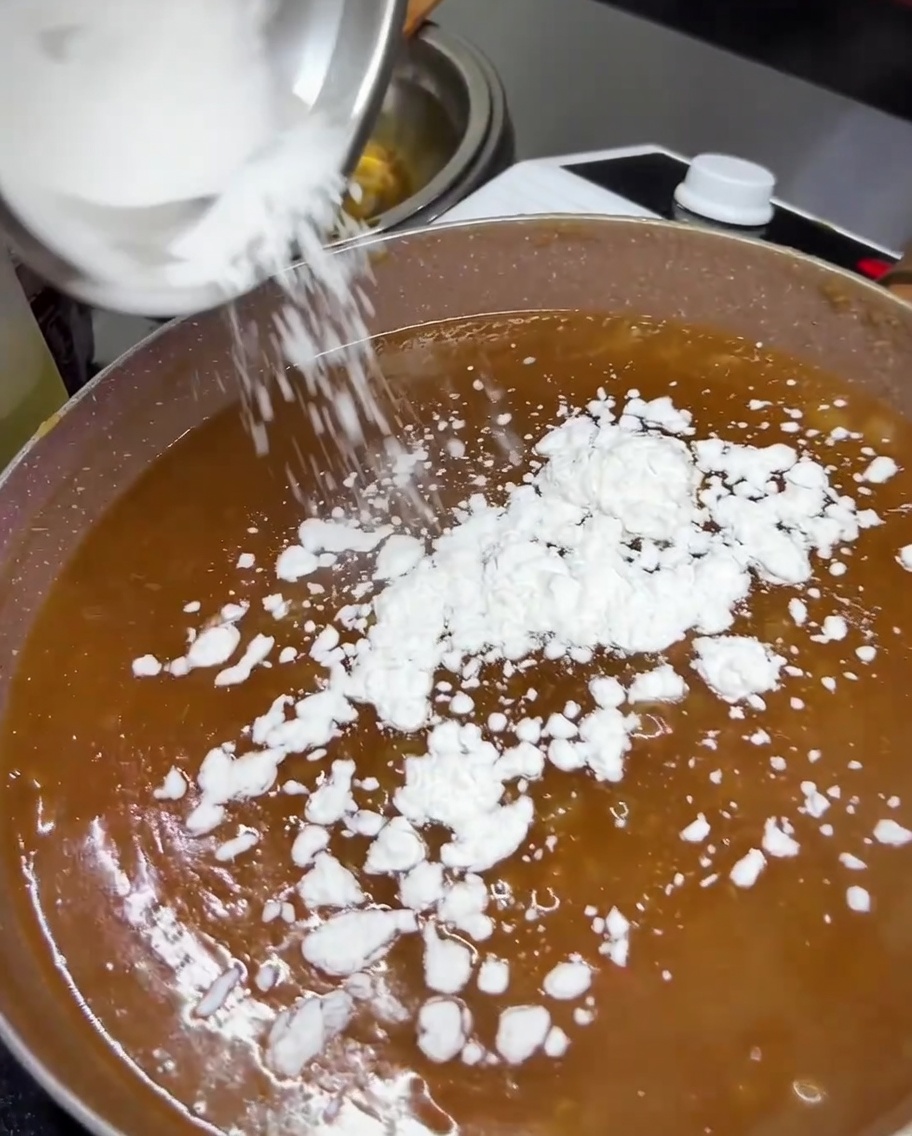 Tapioca starch being added to the simmering teriyaki sauce in a pan.