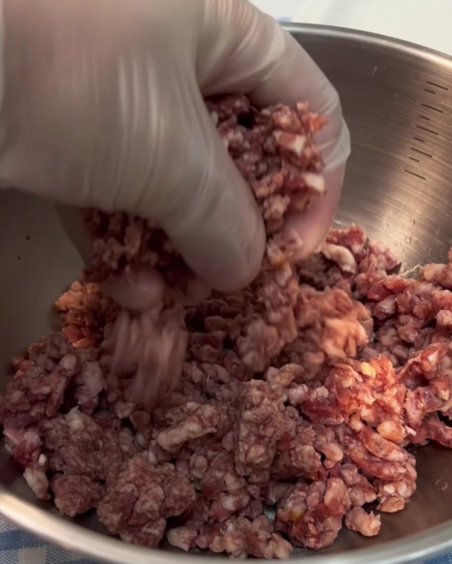 A close-up view of a gloved hand shaping fresh ground beef into a compact ball.