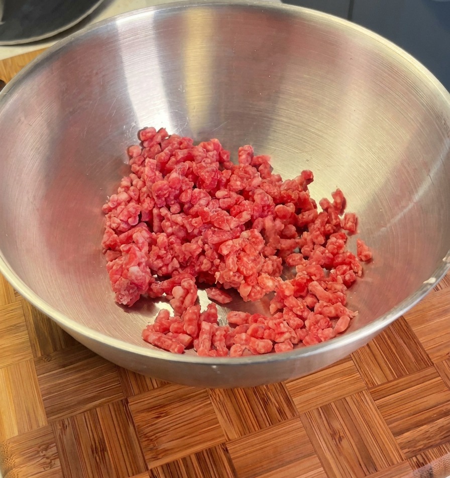 Ground beef in a metal bowl ready to be seasoned with shallots, salt, and black pepper.