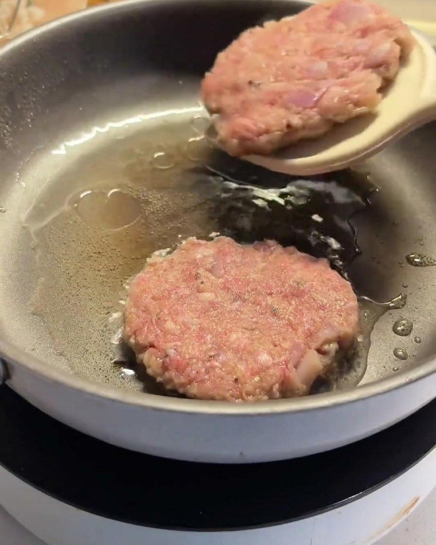 A spatula flipping a partially cooked hamburger patty in the pan.