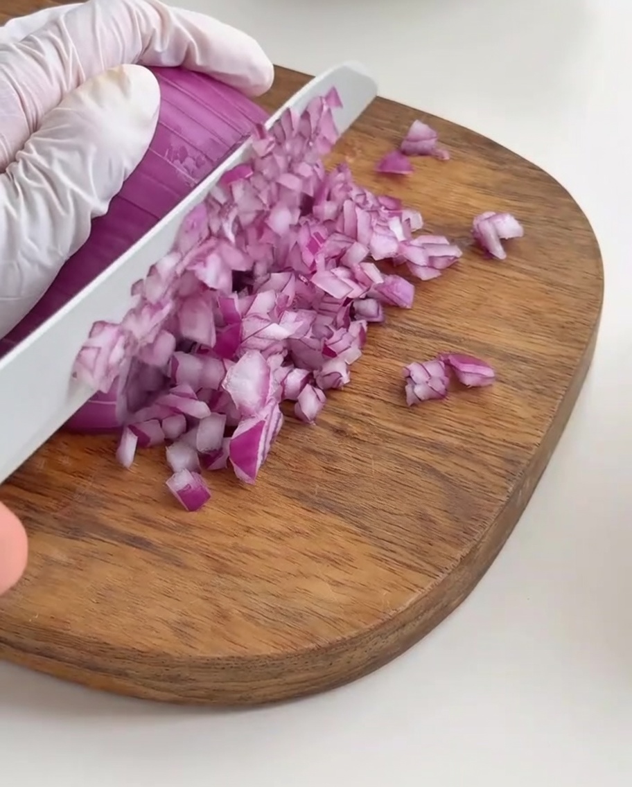 Finely diced red onion pieces neatly arranged on a wooden cutting board.