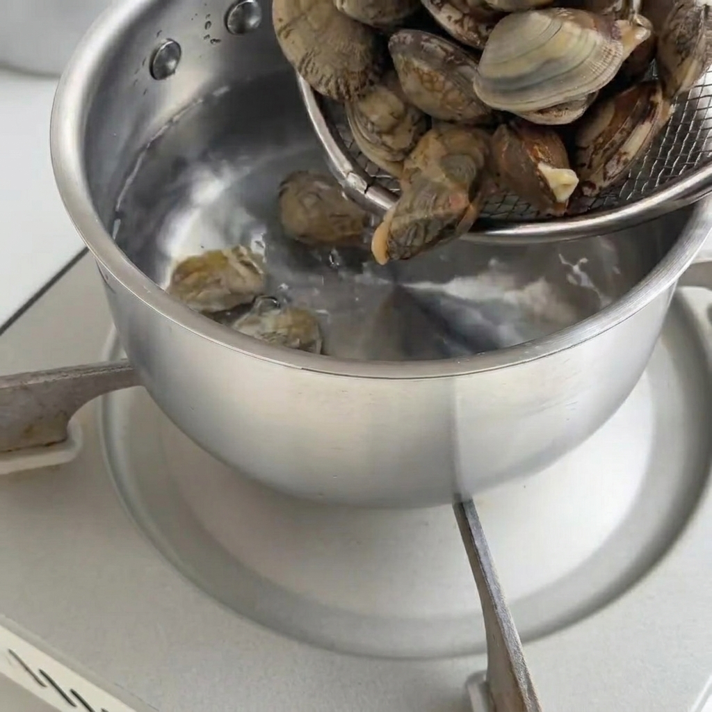 Fresh clams boiling in a pot until the shells open.