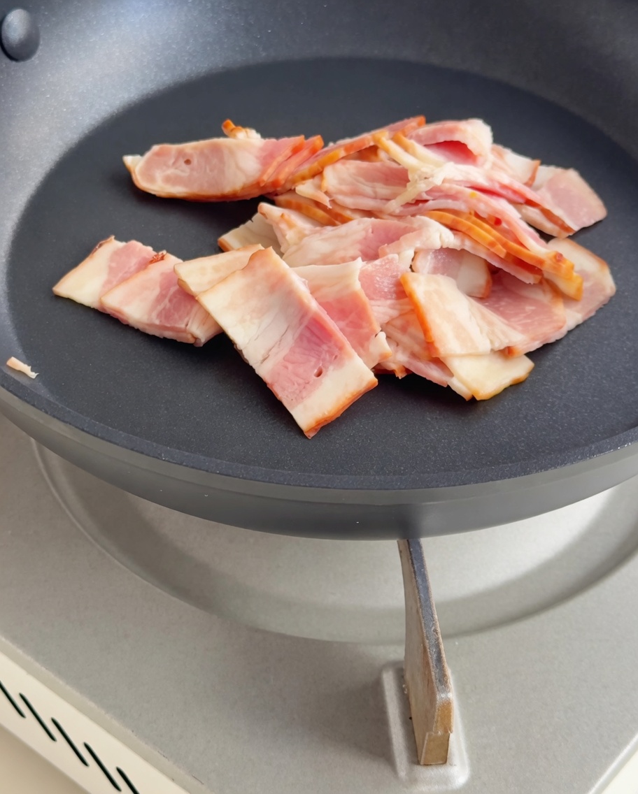 Small pieces of bacon frying in a pan until they are crispy and golden.