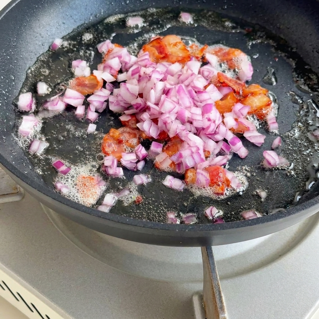 Diced onions, celery, and potato cubes sautéing in a pan with crispy bacon bits.