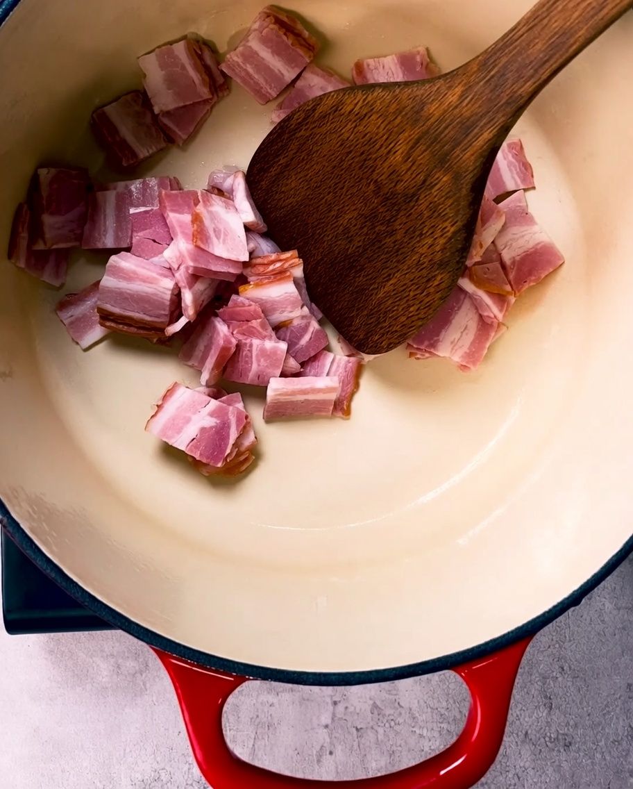 Crispy golden-brown bacon pieces being fried in a large enameled cast iron pot.