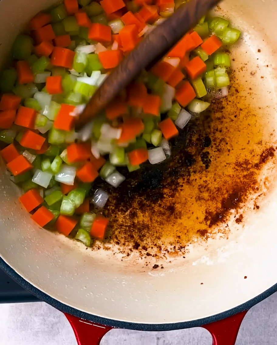 Onions, celery, and carrots sautéing in a pot with rendered bacon fat.