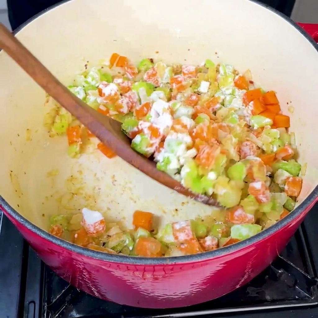 Flour being added to the pot of sautéed vegetables and stirred thoroughly.