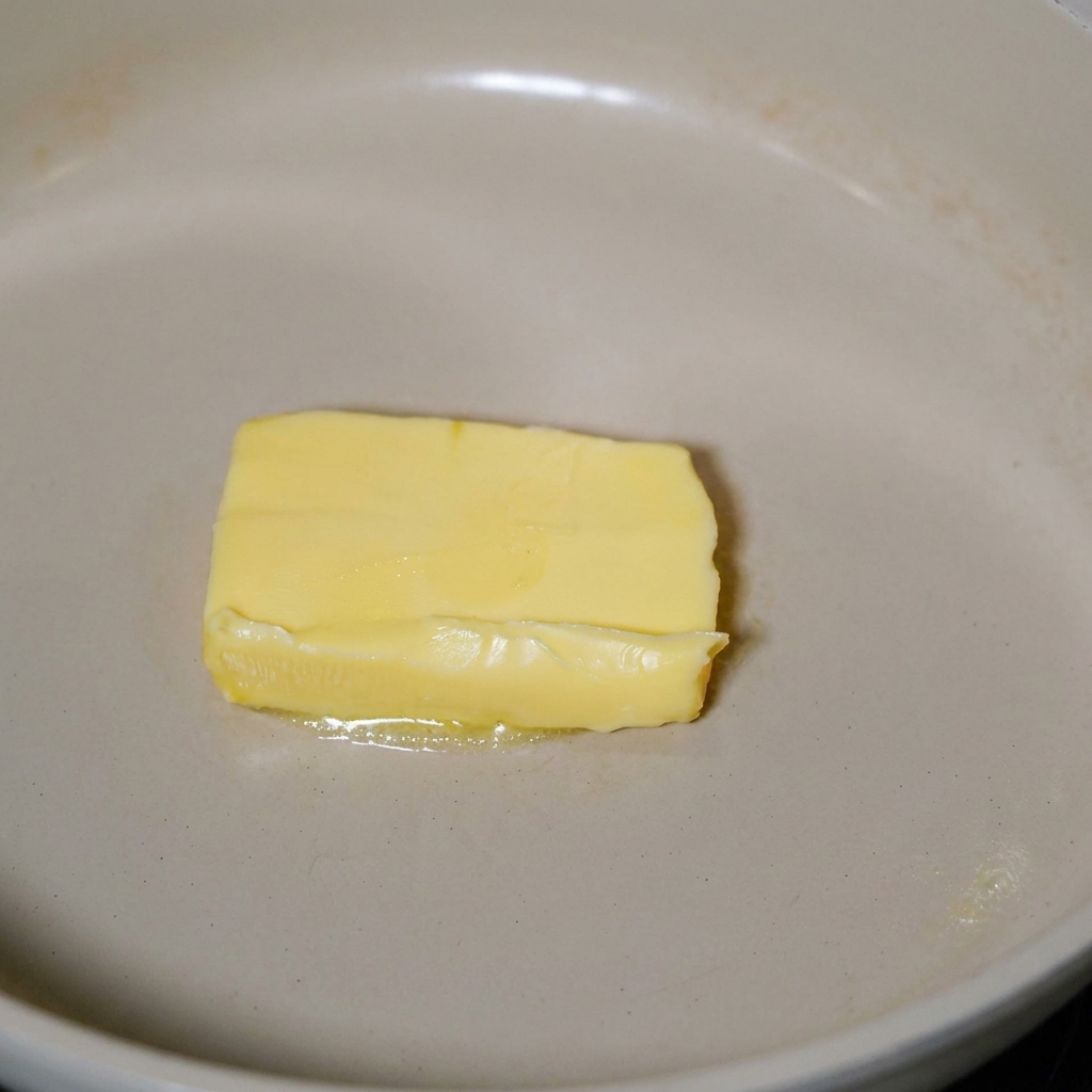 Bacon frying in melted butter in a skillet.