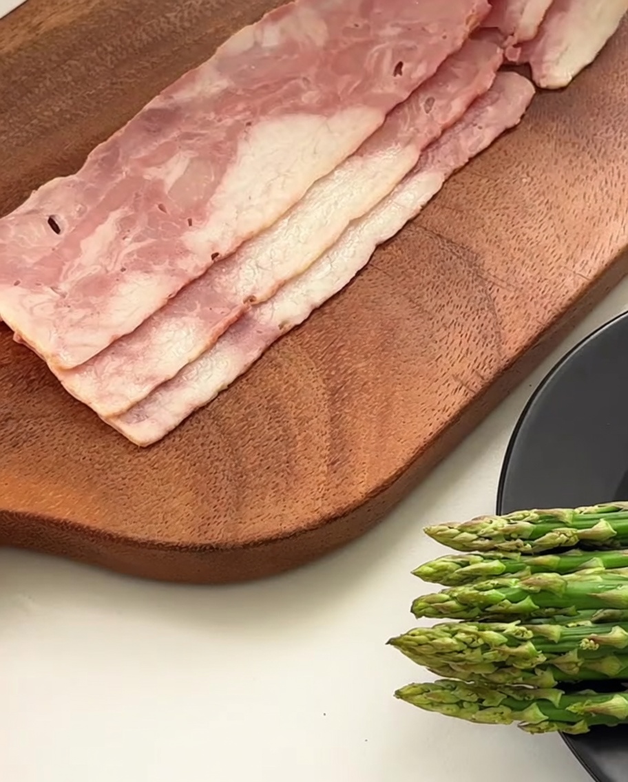 Close-up of a knife cutting bacon slices into smaller pieces on a wooden surface.