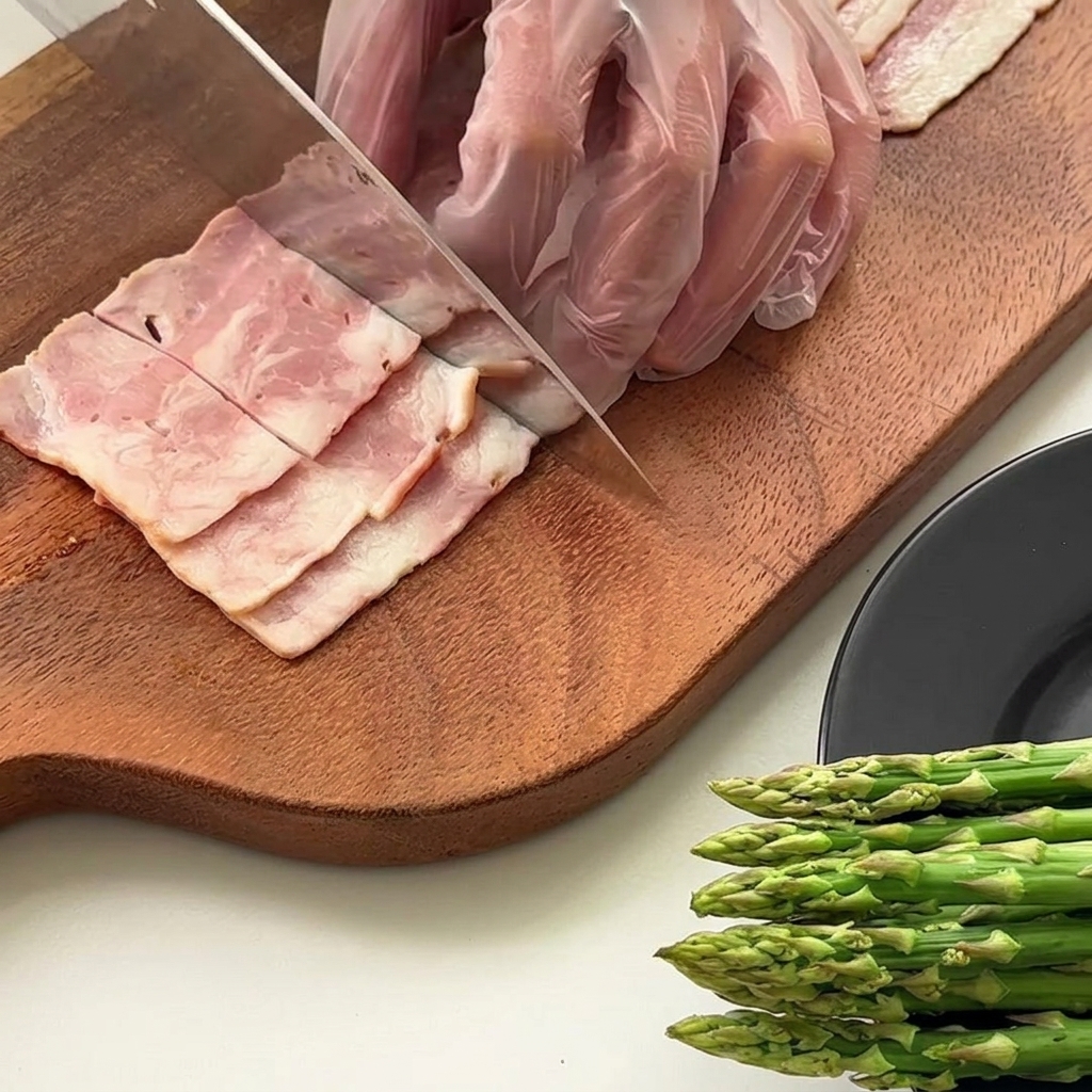Asparagus stalks being cut into equal lengths on a wooden cutting board.