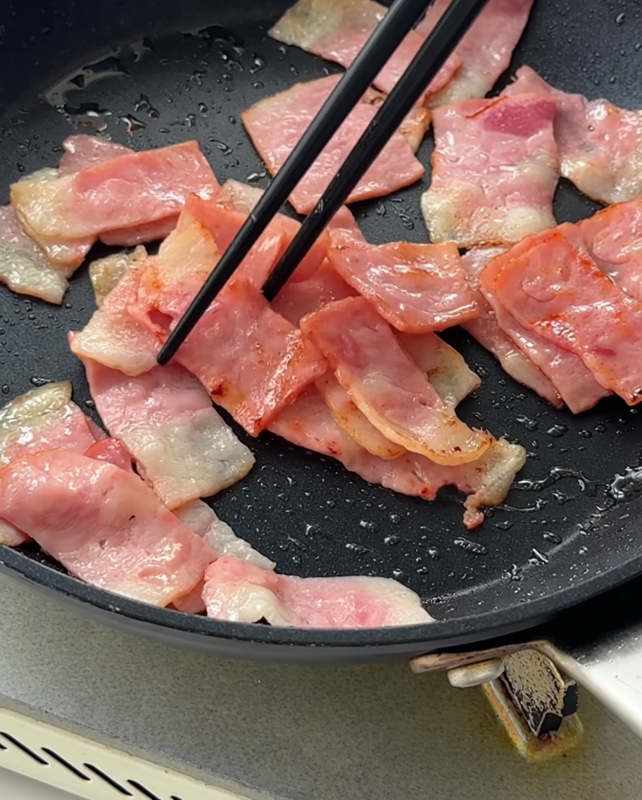 Diced purple onions being stirred into the pan with the browned bacon.