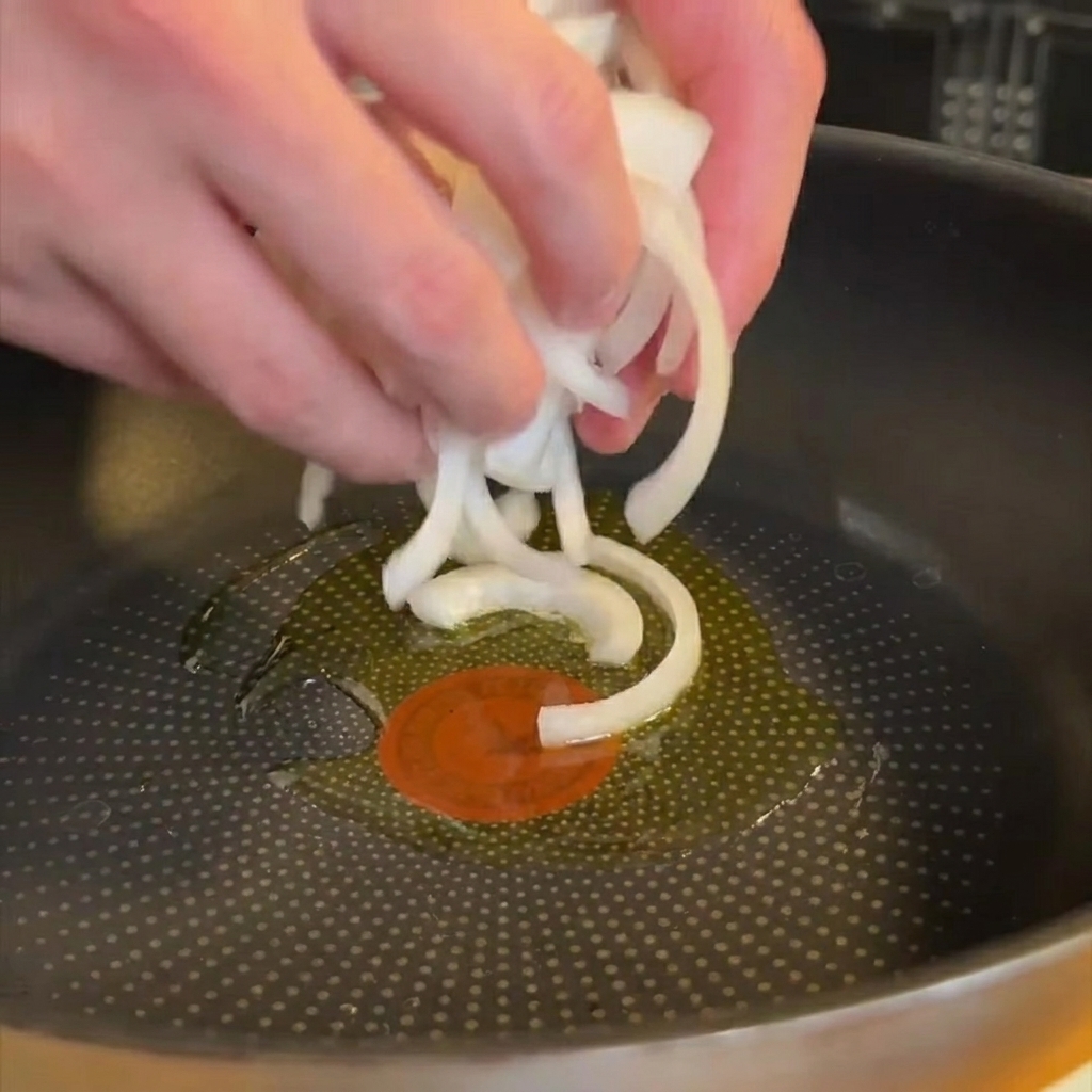Thinly sliced onions softening in a pan with shimmering olive oil.