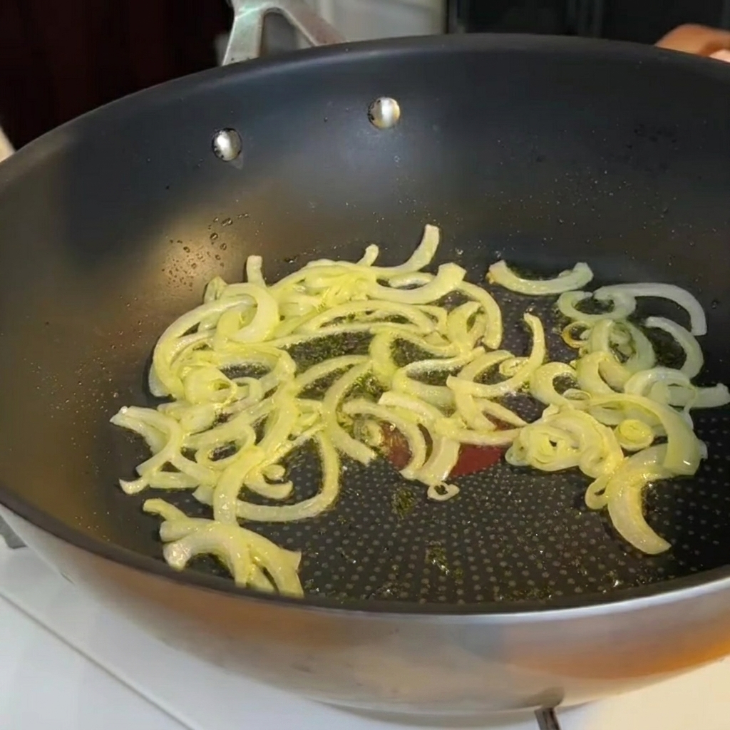 Chopped asparagus stems being added to a pan containing softened sautéed onions.
