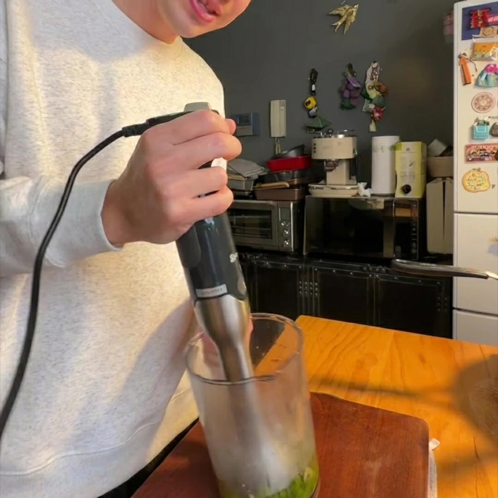 An immersion blender processing cooked asparagus and onions in a glass container until smooth.
