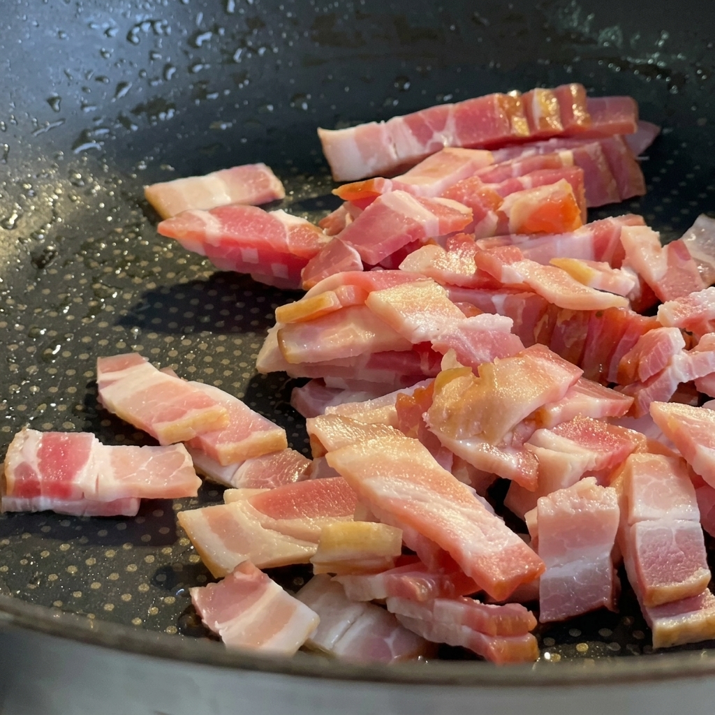 Bacon pieces frying in a pan until browned and crispy.