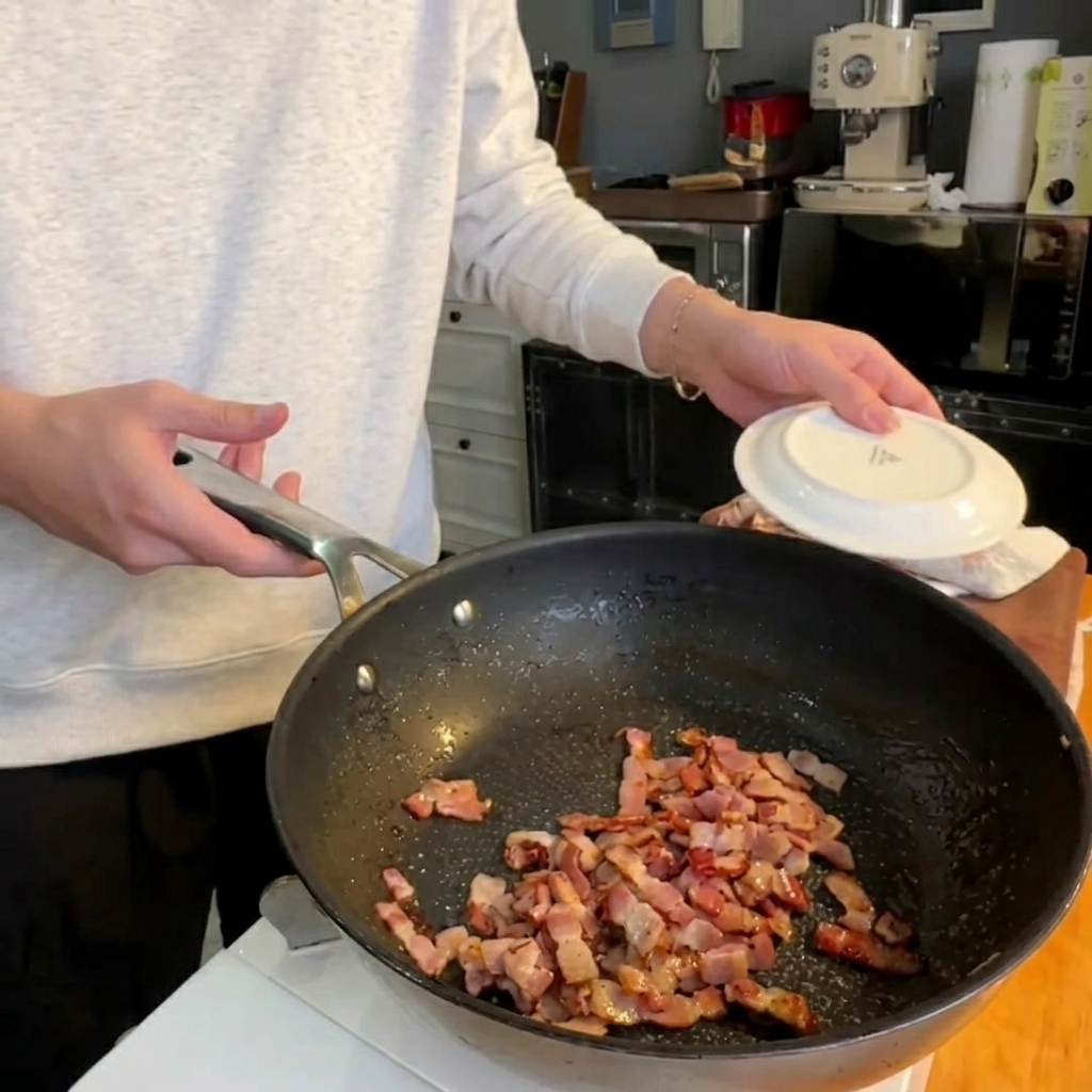 Fresh asparagus tops frying in a pan alongside crispy bacon pieces.
