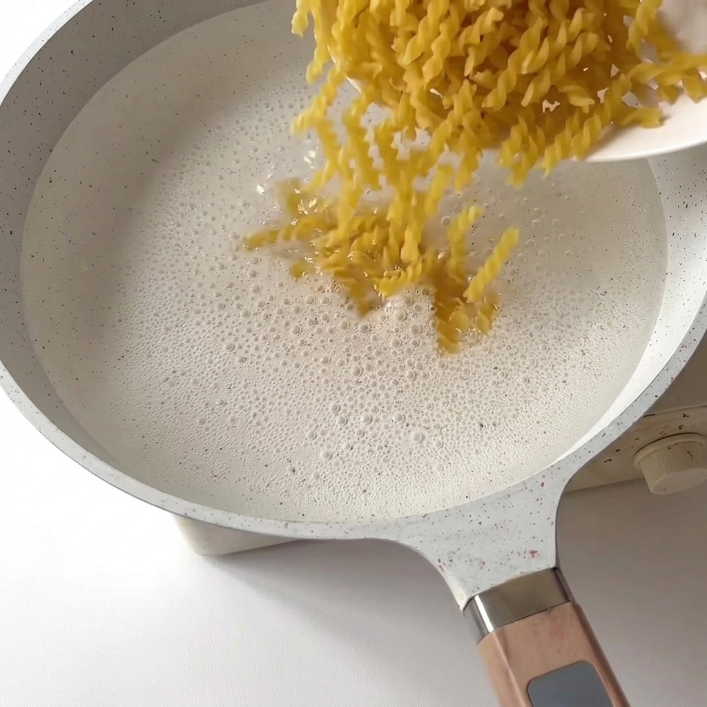 Fusilli pasta dropping into a pot of bubbling boiling water.