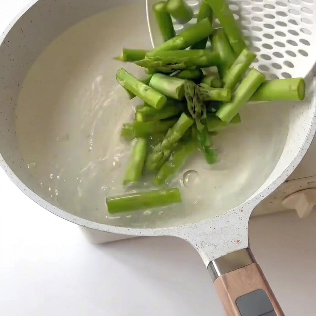 Asparagus pieces being blanched in boiling water using a slotted spoon.