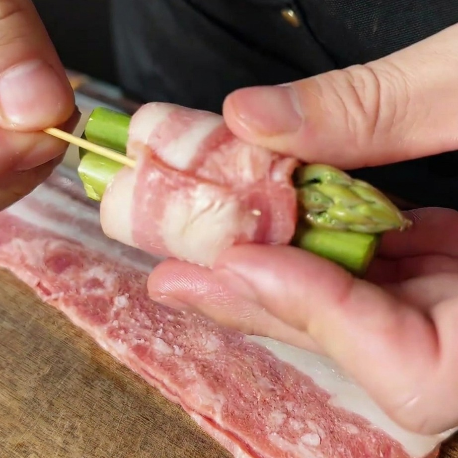 A bacon-wrapped asparagus bundle being secured with a small wooden toothpick.