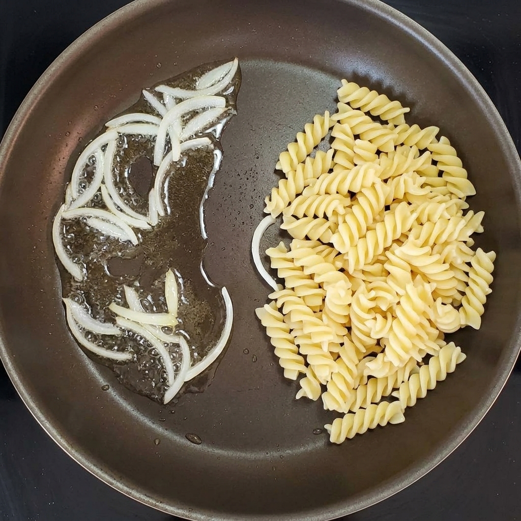 Spiral pasta being mixed with sautéed onions in a cooking pan.