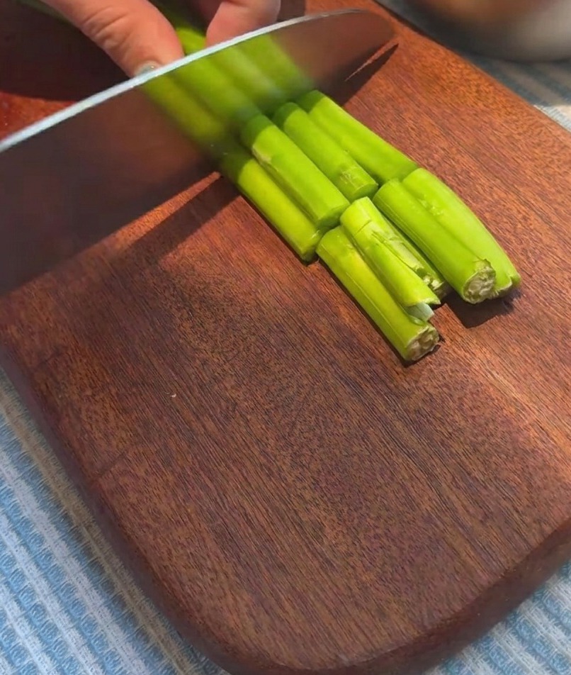 Fresh asparagus spears being sliced into uniform pieces on a wooden cutting board.