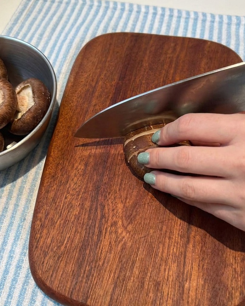 Fresh mushrooms being carefully sliced into thin pieces on a wooden cutting board.