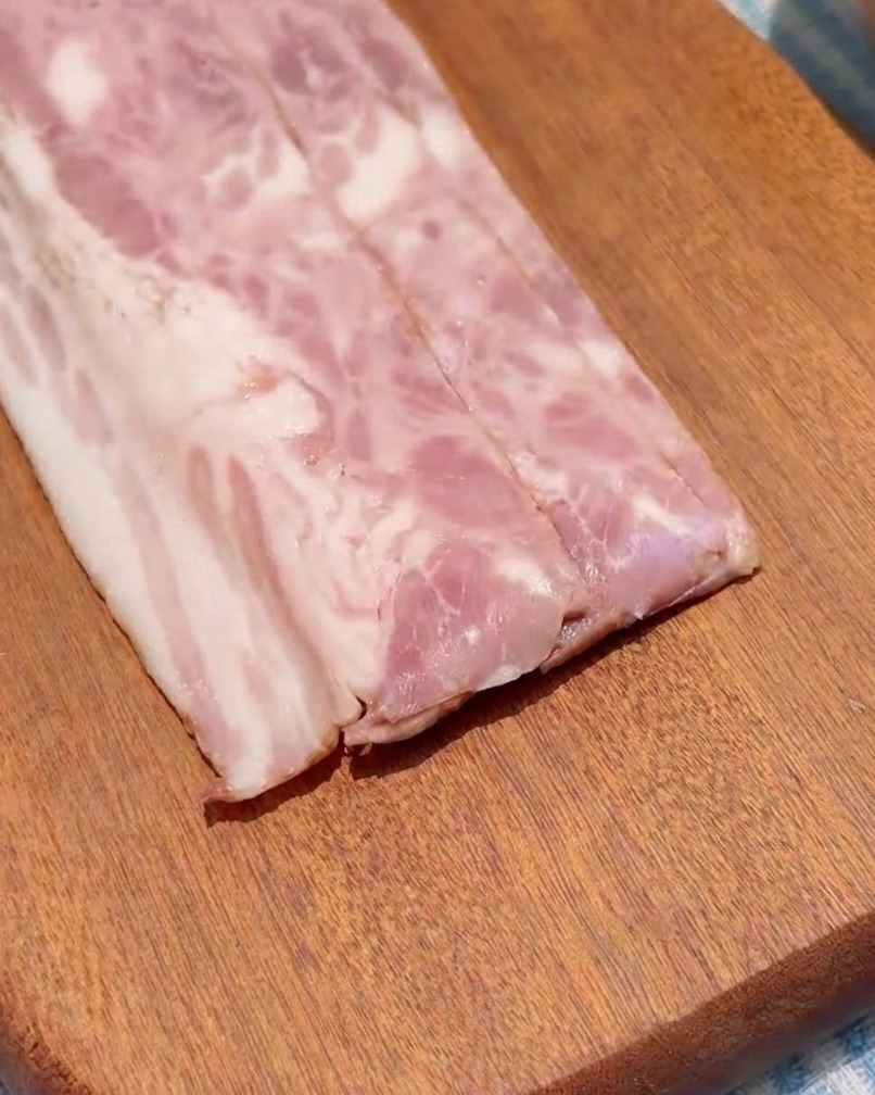 Strips of bacon being chopped into even squares on a wooden cutting board.