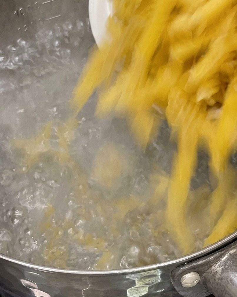 Raw pasta being dropped into a pot of bubbling boiling water.