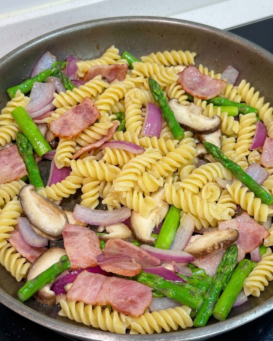 Pasta mixing with vegetables and bacon in a pan, being seasoned with black pepper and soy sauce.