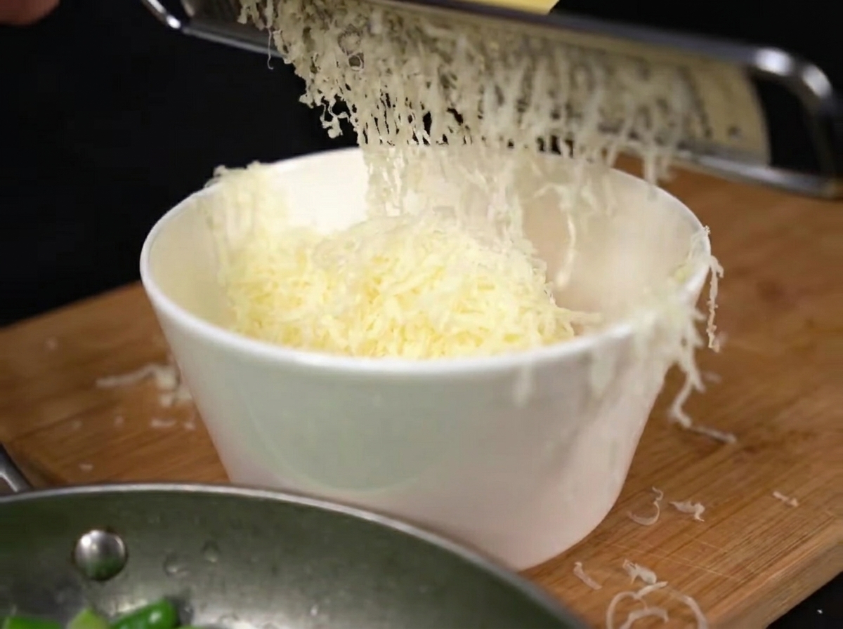 Freshly grated parmesan cheese falling in a heap onto the egg yolks in a mixing bowl.