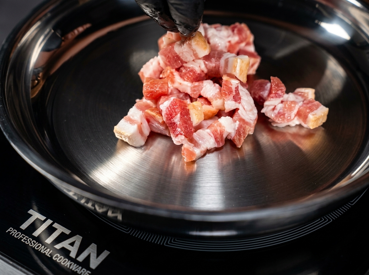 Bacon pieces browning in a hot metal pan, stirred with black-tipped tongs.