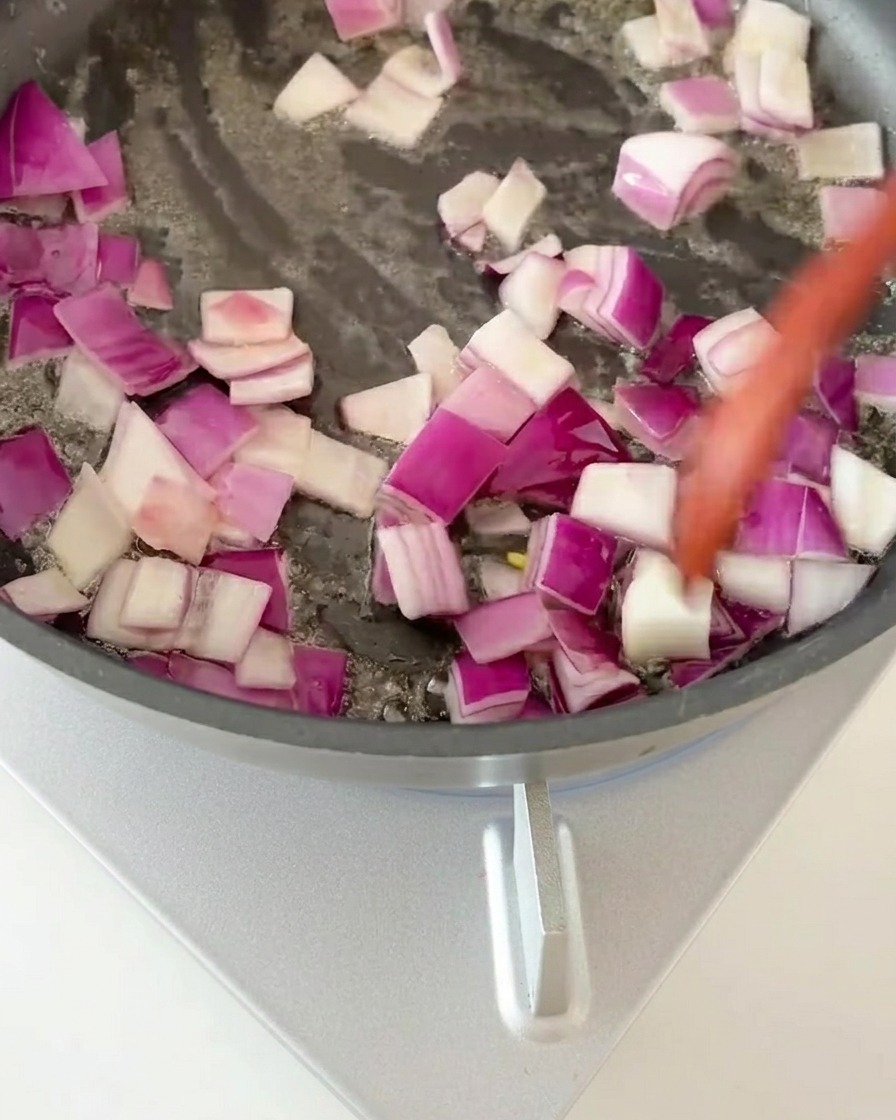 Red onion cubes being stirred in a hot frying pan until fragrant.