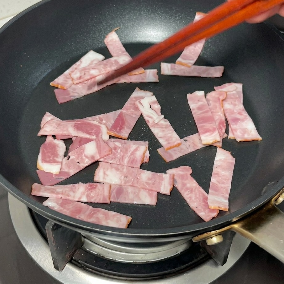 Bacon strips frying in a pan until they reach a golden brown color.