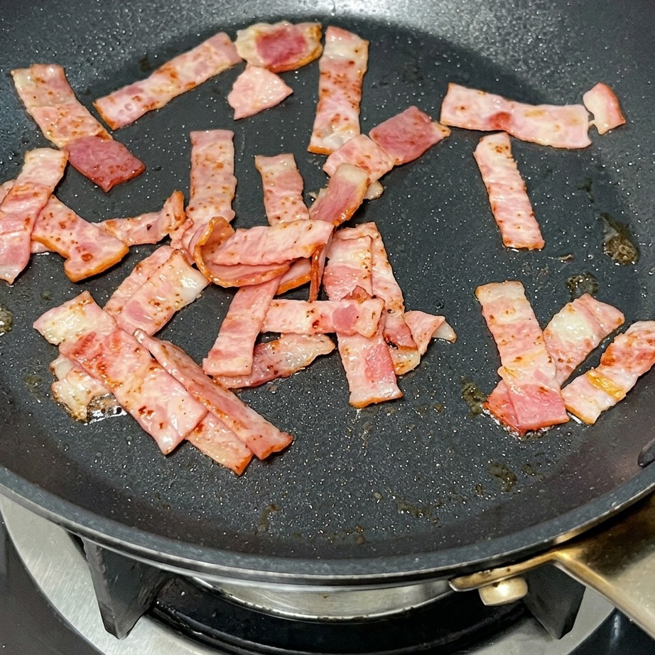 A knob of butter melting in a pan with fried bacon pieces.