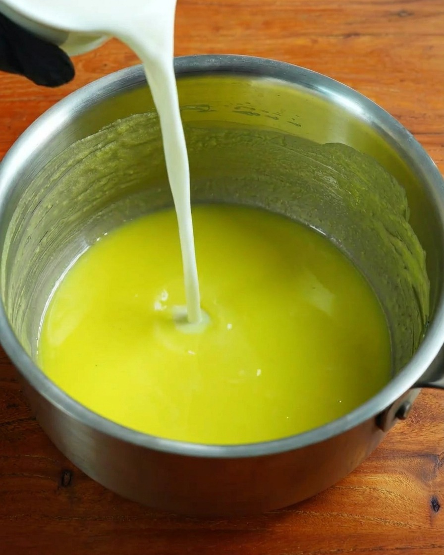 Warm milk being poured into the roux base while whisking.