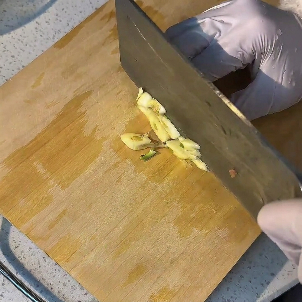 Fresh garlic cloves being minced on a wooden cutting board.