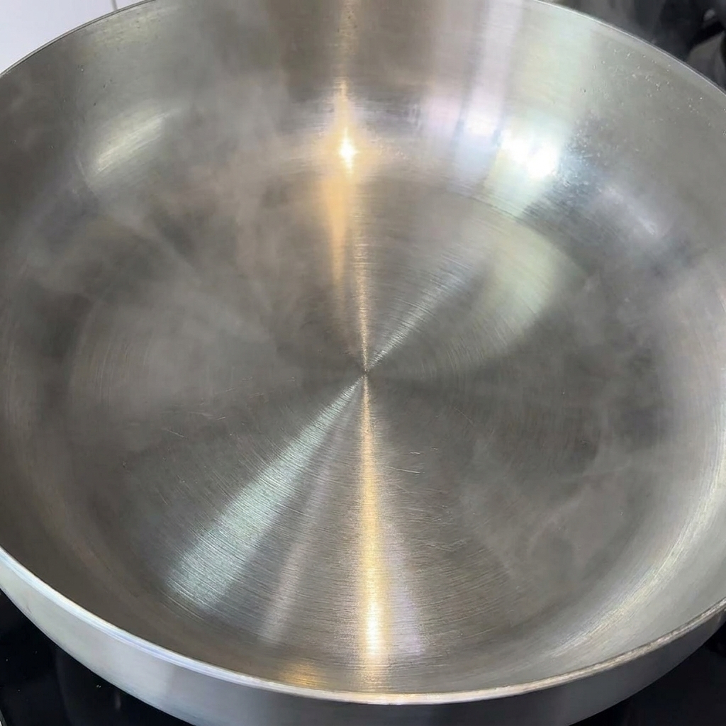 A cube of butter melting in a large, clean stainless steel pan.